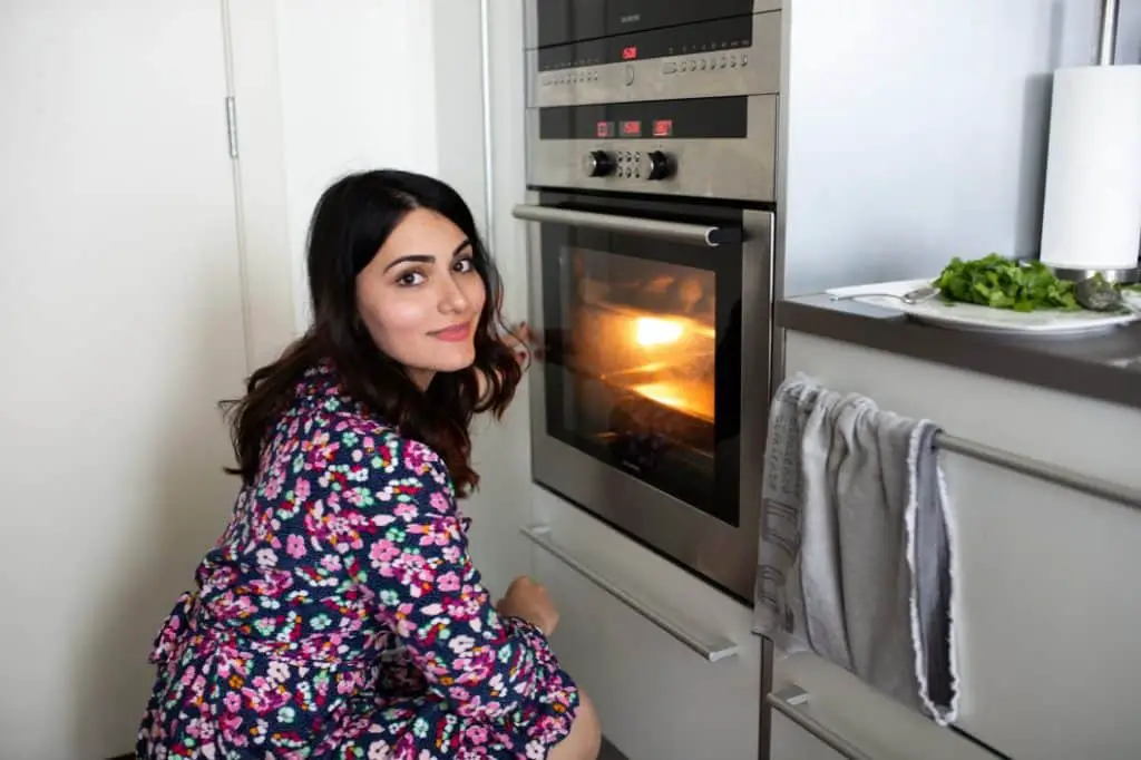 Lady in front of her oven waiting for a meal to finish.